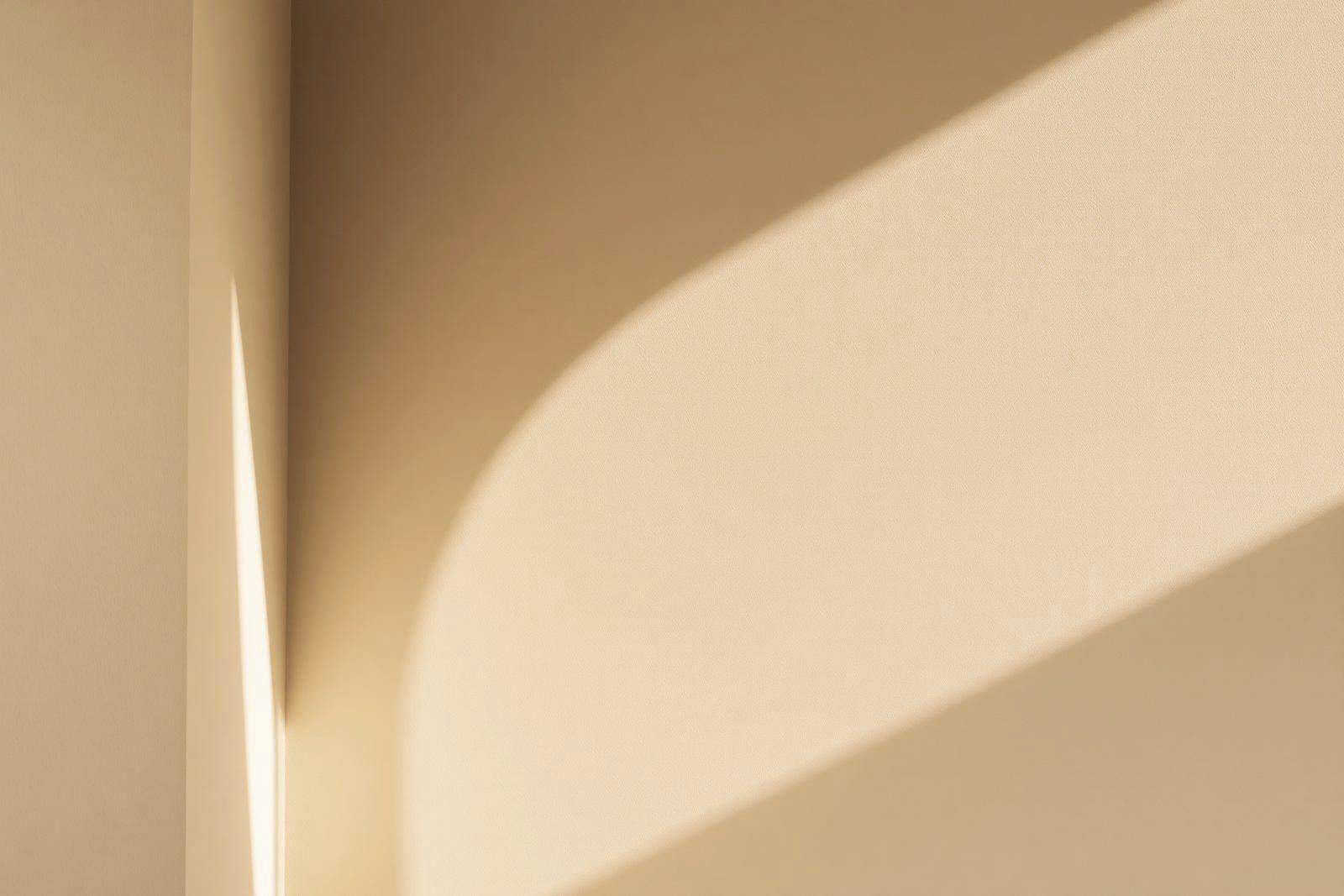 A soft arch of shadow moving across a warm limewash wall