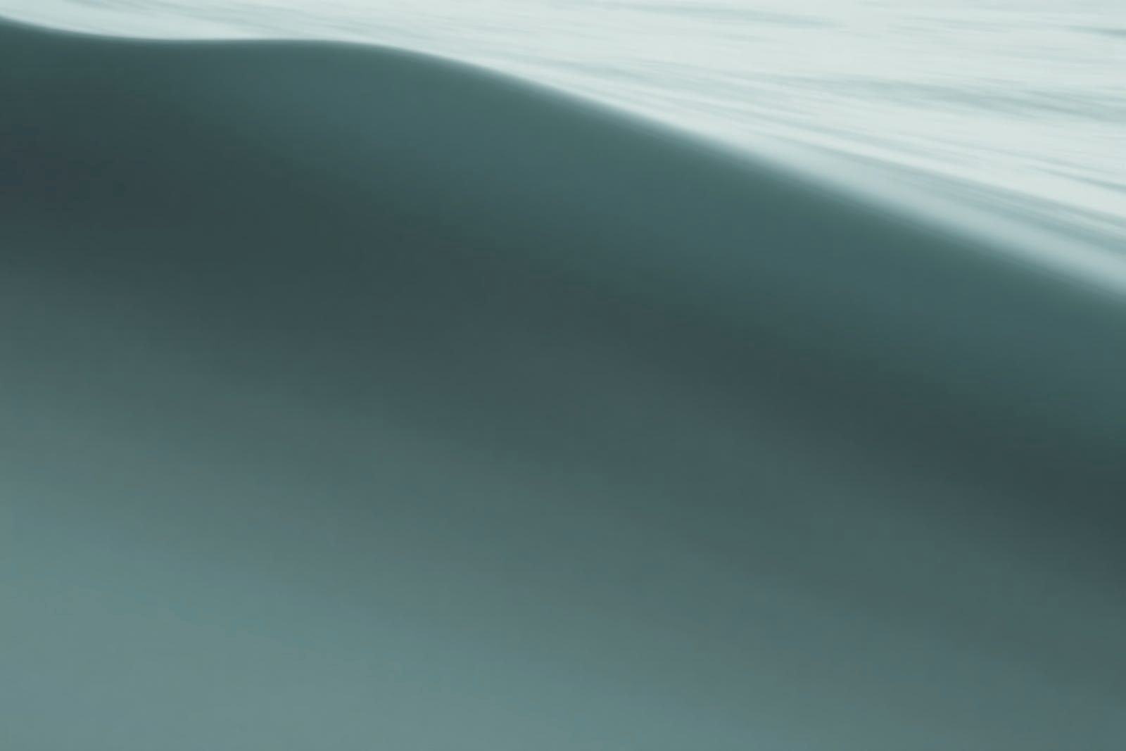 The smooth face of a slow ocean swell rising in flat light